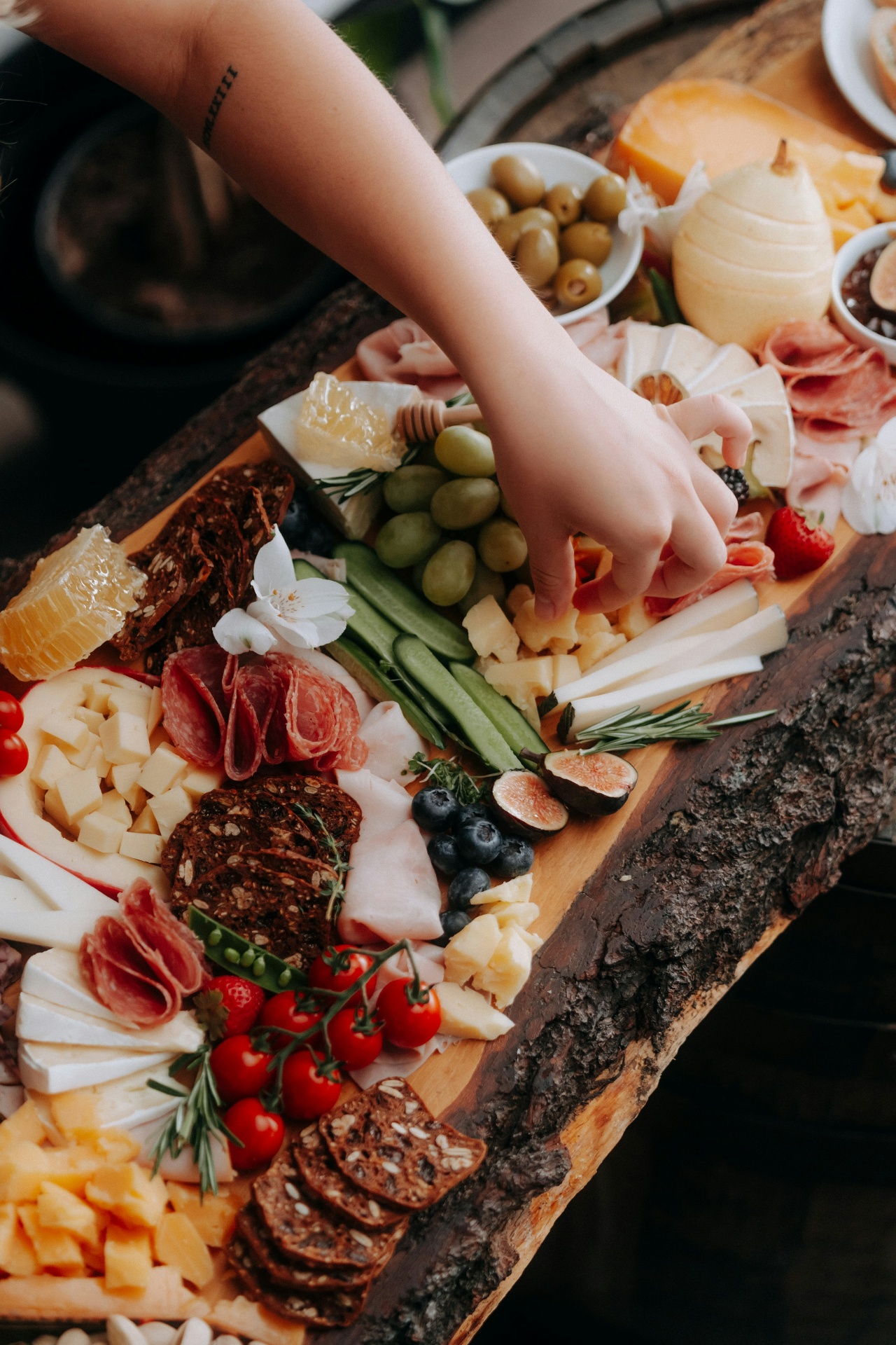 A guest reaching for an artisan charcuterie board styled with figs, honeycomb, and Colorado florals.